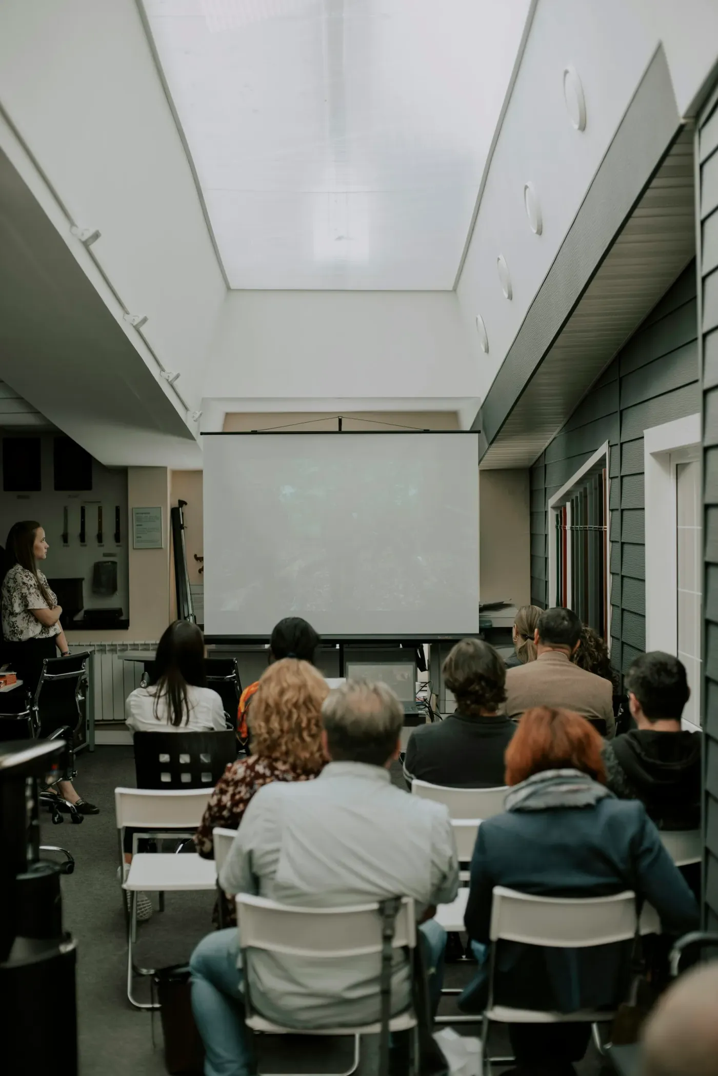 A small hall, rows of chairs, people watching a film on a projector screen at the front.