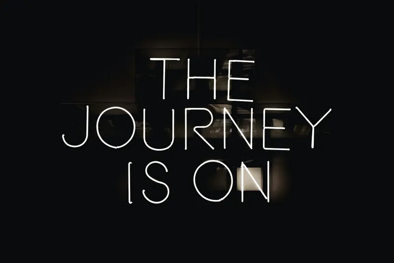 A neon sign glowing in a dark room, reading “The journey is on.”