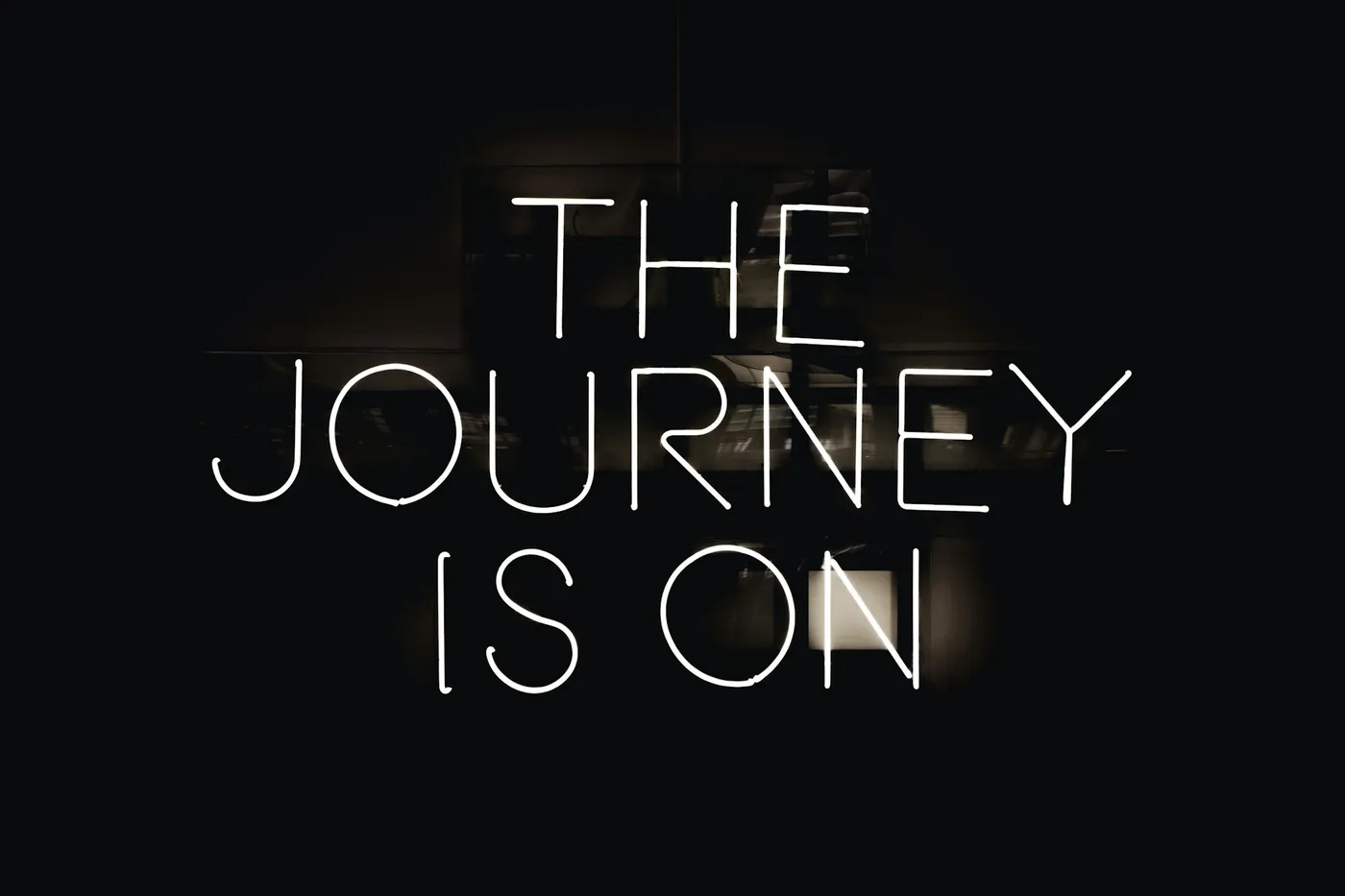 A neon sign glowing in a dark room, reading “The journey is on.”